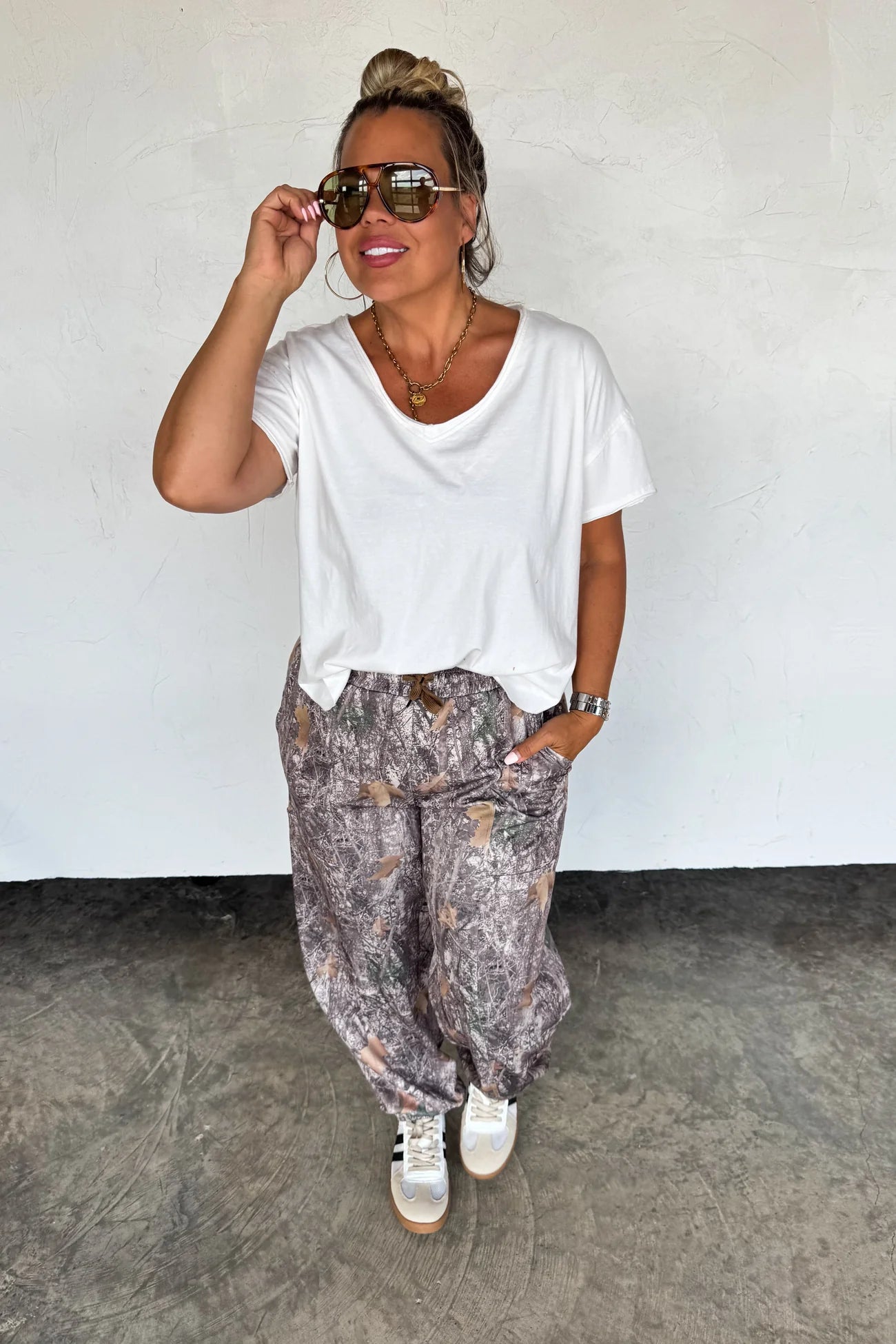 Woman wearing a white t-shirt and patterned pants against a plain background