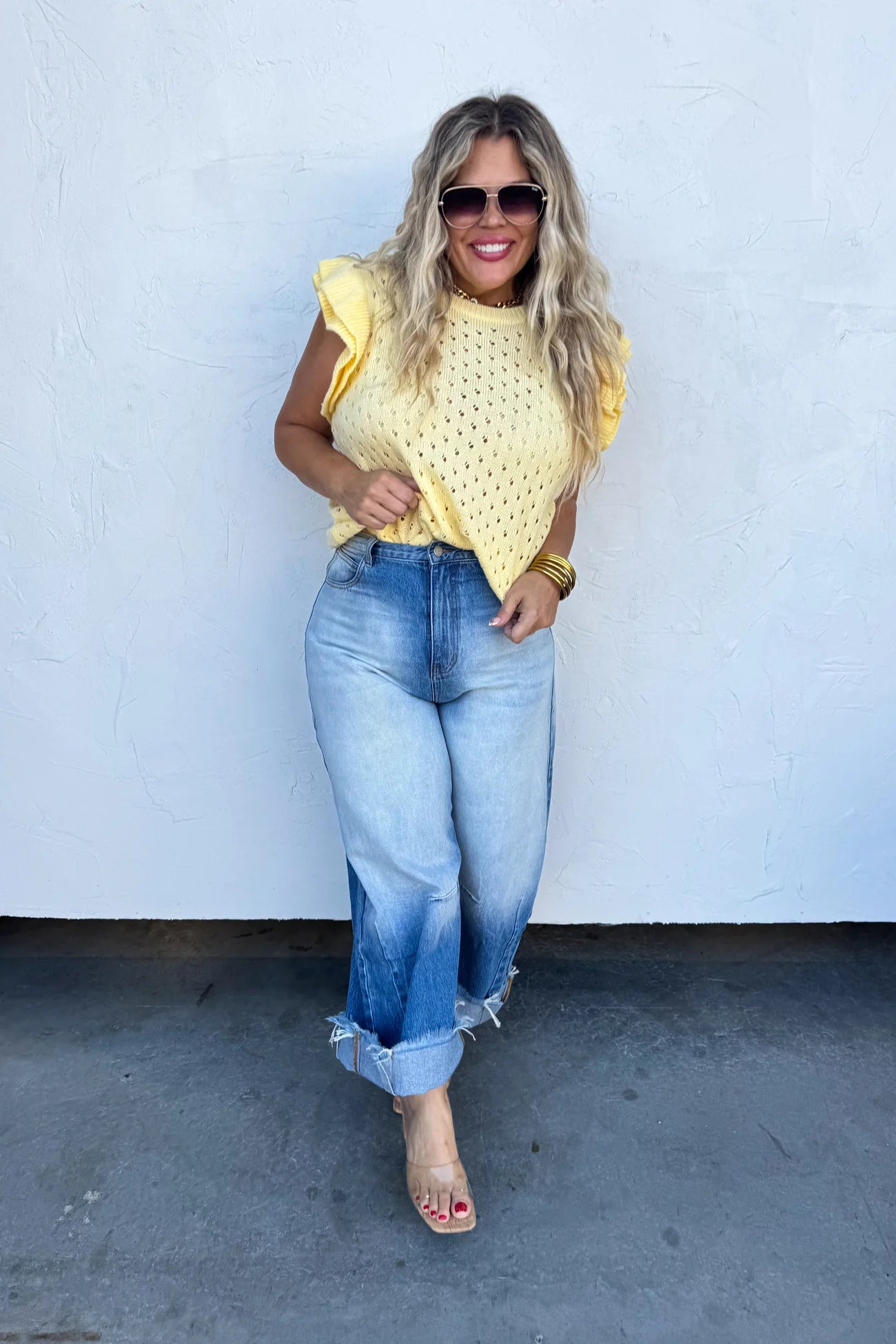 Woman wearing a yellow top and blue jeans against a white wall.