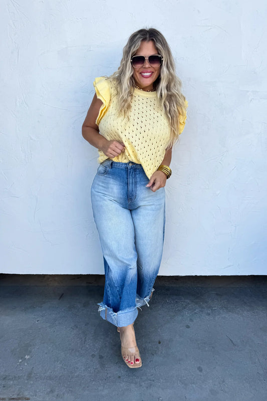 Woman wearing a yellow top and blue jeans against a white wall.
