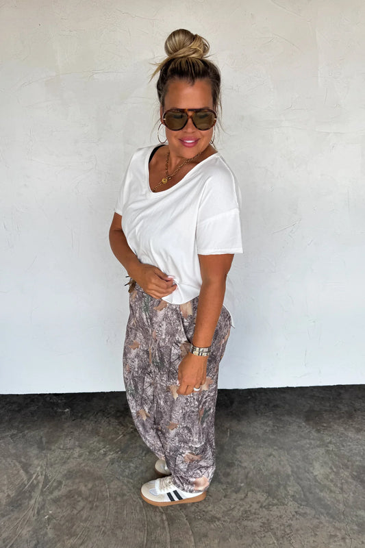 Woman wearing a white t-shirt and patterned pants against a plain background